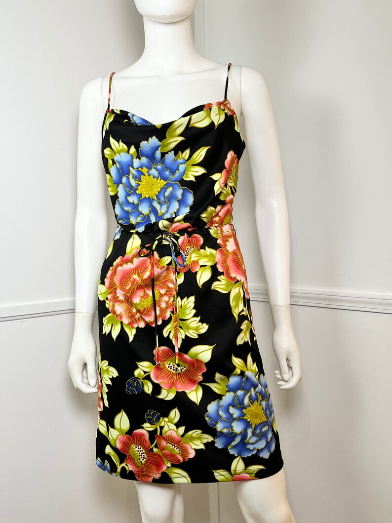 May include: A black sleeveless dress with a floral print featuring large pink, blue, and yellow flowers. The dress has a cowl neck and a drawstring waist.