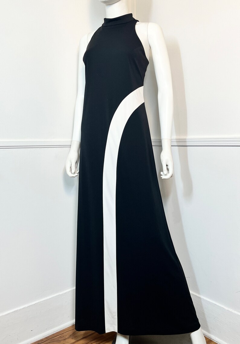 May include: A black maxi dress with a white curved design on the side. The dress has a high neck and sleeveless design.