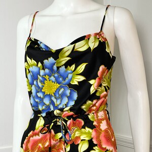 May include: A black sleeveless jumpsuit with a floral print featuring blue, pink, and yellow flowers. The jumpsuit has a cowl neck and a drawstring waist.
