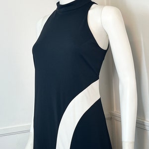 May include: A black sleeveless dress with a white curved design on the side. The dress has a high neck and a fitted silhouette.