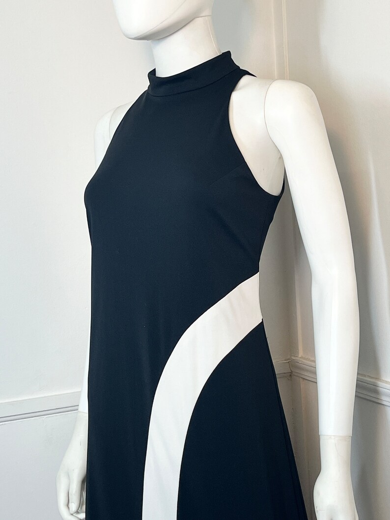 May include: A black sleeveless dress with a white curved design on the side. The dress has a high neck and a fitted silhouette.