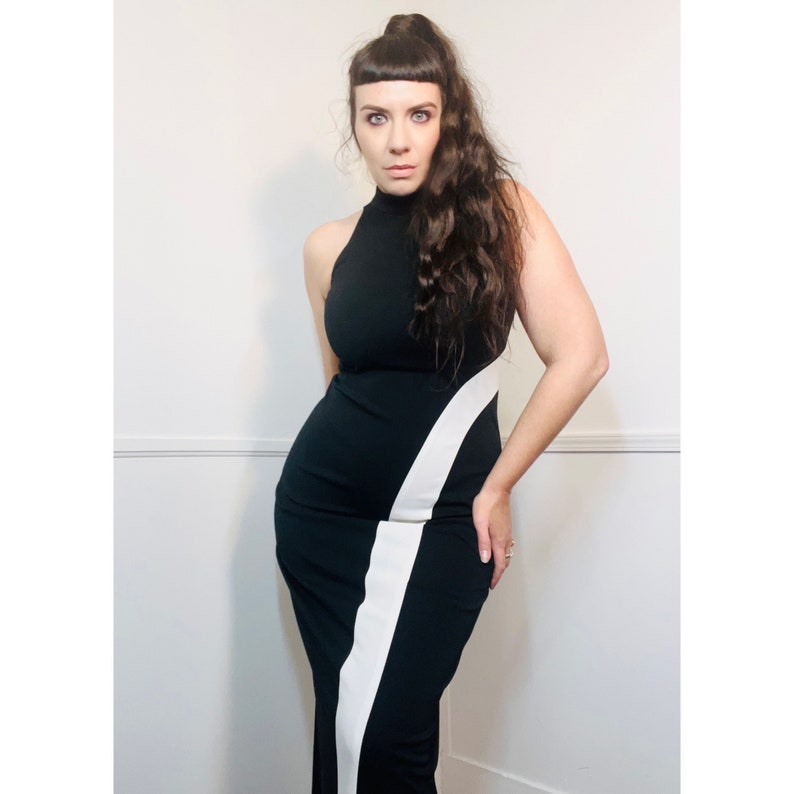 May include: A woman wearing a black and white dress with a high neckline and a diagonal white stripe. The dress is fitted and has a long skirt.