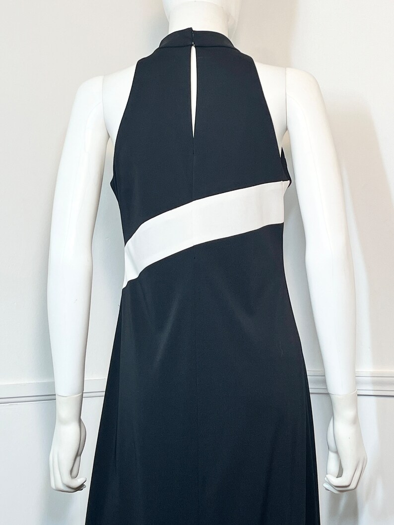 May include: A black sleeveless dress with a white stripe across the chest. The dress has a halter neckline and a back zipper.