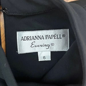 May include: A black dress with a silver tag that reads "Adrianna Papell Evening" and a size 6 tag.