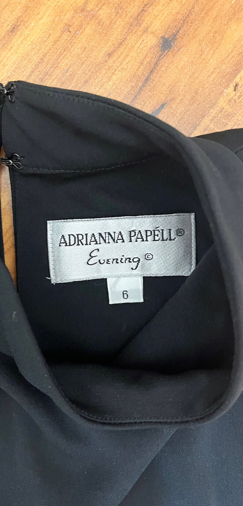 May include: A black dress with a silver tag that reads "Adrianna Papell Evening" and a size 6 tag.