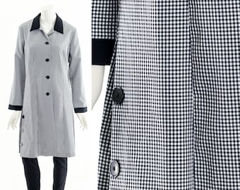 May include: A long coat in a black and white gingham pattern, featuring a black collar, cuffs, and buttons. The coat is fastened with buttons down the front and on the side. It is displayed on a mannequin with black leggings.