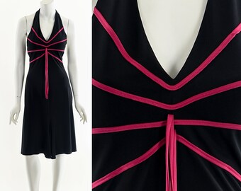 May include: Black halter dress with pink trim and a tie detail. The dress features a V-neckline and a knee-length hemline. The pink trim creates a striking contrast against the black fabric, adding a pop of color to the design.