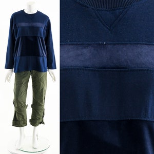 May include: A navy blue long-sleeved sweatshirt with a contrasting dark blue velvet panel across the chest. The sweatshirt has a crew neck and a relaxed fit.