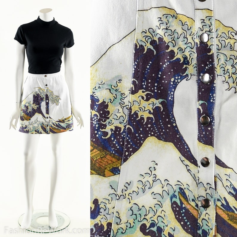 May include: A white denim mini skirt with a printed image of the Great Wave off Kanagawa by Katsushika Hokusai. The skirt has a button closure and a relaxed fit.