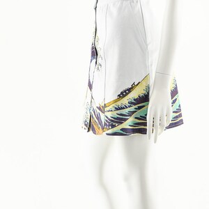 May include: A white skirt with a blue and yellow wave print. The skirt has a button closure and a high waist. The skirt is being modeled on a white mannequin.