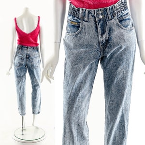 May include: Light blue acid wash denim jeans with a high waist and a relaxed fit. The jeans have a faded look and a slightly distressed appearance.