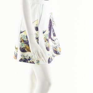 May include: A white skirt with a black and blue wave print. The skirt is pleated and has a high waist. The skirt is being modeled on a white mannequin.