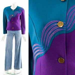 May include: A purple and teal blazer with a wavy design on the front. The blazer has gold buttons and a collar.