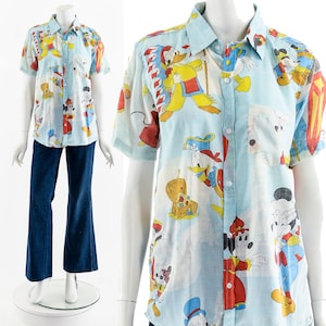 May include: A light blue short-sleeved button-down shirt with a colorful all-over print of Disney characters, including Mickey Mouse, Donald Duck, and Goofy.
