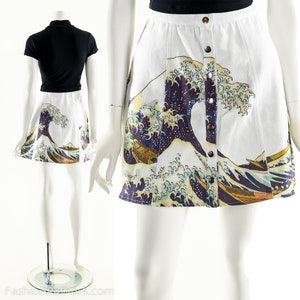 May include: A white mini skirt with a button-up front closure. The skirt features a colorful print of the Great Wave off Kanagawa by Katsushika Hokusai.