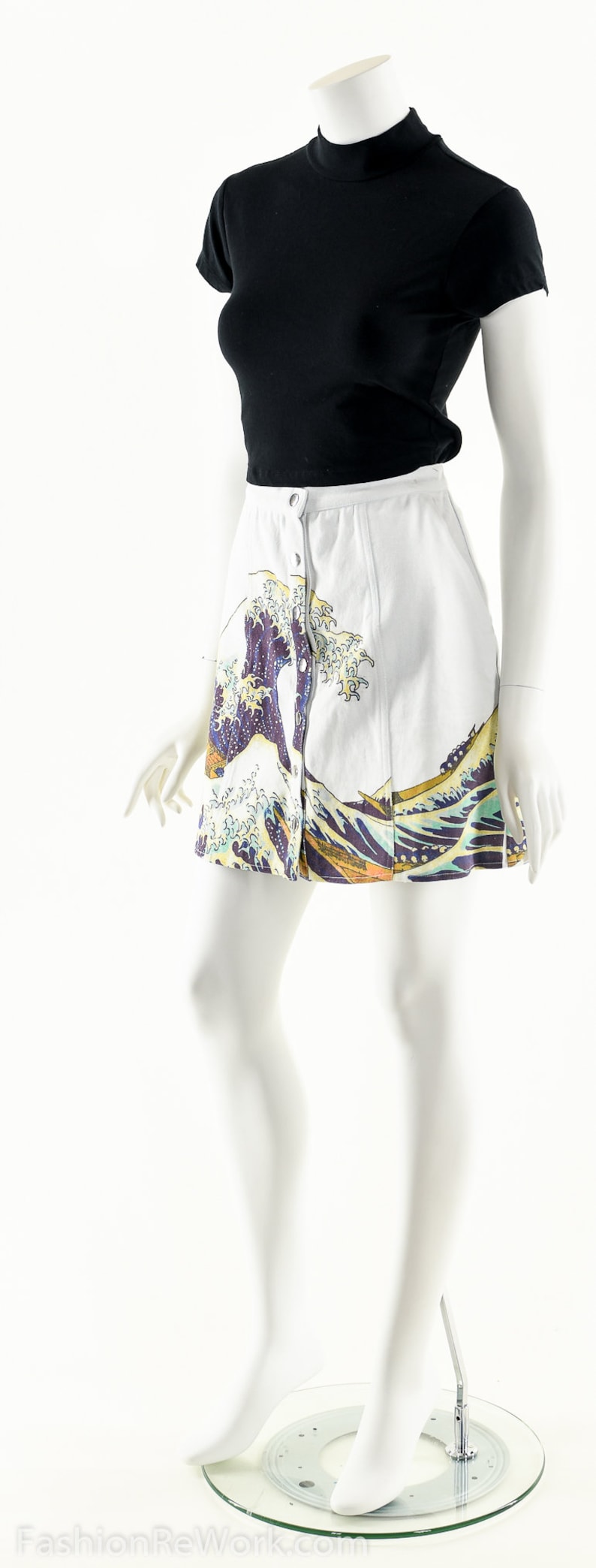 May include: A white skirt with a blue and yellow wave print and a button closure. The skirt is being modeled on a white mannequin.
