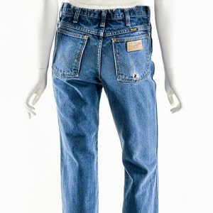 Puede incluir: Un par de pantalones vaqueros azules con un parche de cuero marr&oacute;n claro en el bolsillo trasero que dice "Wrangler".