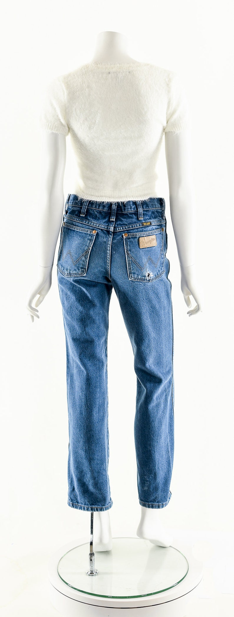 Puede incluir: Un par de pantalones vaqueros azules con un parche de cuero marr&oacute;n claro en el bolsillo trasero que dice "Wrangler".