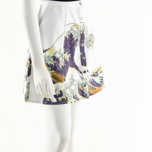 May include: A white skirt with a blue and yellow print of a wave. The skirt has a button closure and is worn on a white mannequin.