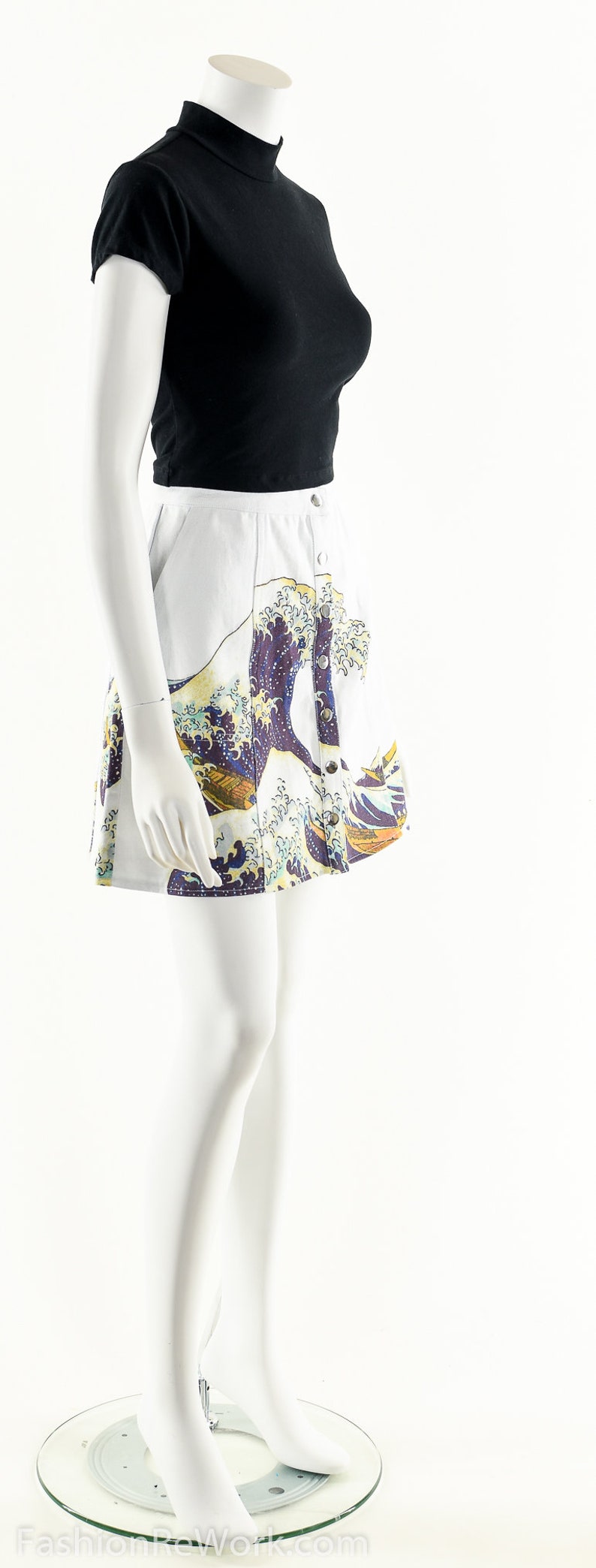 May include: A white skirt with a blue and yellow print of a wave. The skirt has a button closure and is worn on a white mannequin.