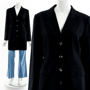 Könnte beinhalten: Ein schwarzer Blazer mit klassischem Design, mit Reverskragen, vier Knöpfen und zwei Vordertaschen. Der Blazer wird auf einer Schaufensterpuppe mit hellblauen Jeans präsentiert. Das Kleidungsstück hat eine taillierte Passform und eine professionelle Ästhetik.