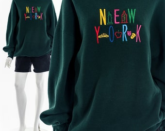 May include: Green sweatshirt with a colorful embroidered design that says "NEW YORK" with icons representing the city, including the Statue of Liberty, a taxi cab, and an apple.