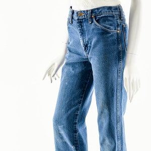 Puede incluir: Un par de pantalones vaqueros azules de mezclilla con cintura alta y piernas rectas. Los pantalones vaqueros est&aacute;n en un maniqu&iacute; blanco.
