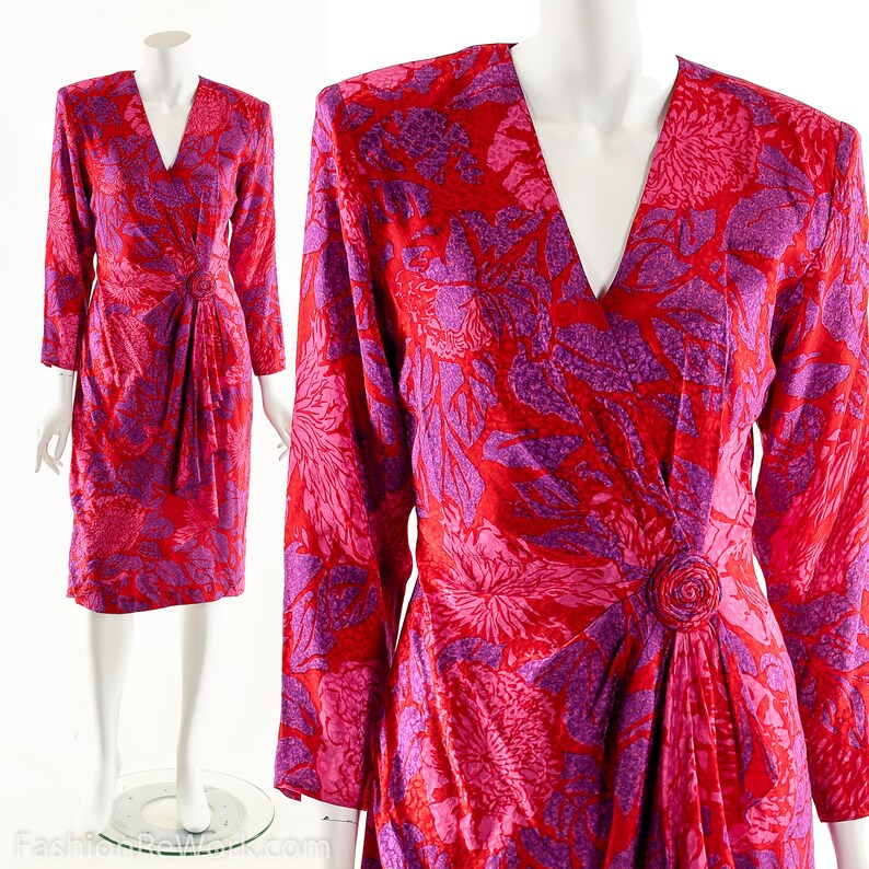 May include: A long-sleeved wrap dress with a V-neckline. The dress is made of a red and purple floral print fabric. The dress has a tie at the waist and a button detail.