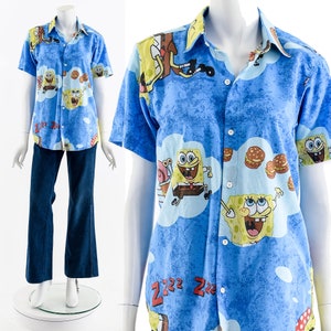 Puede incluir: Una camisa azul de manga corta con botones con un estampado de dibujos animados de Bob Esponja, Patricio Estrella y otros personajes. La camisa tiene un fondo azul claro con nubes blancas y el texto "Zzz Zzz" impreso en ella.