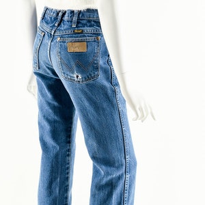 Puede incluir: Un par de pantalones vaqueros azules con un parche de cuero marr&oacute;n en el bolsillo trasero que dice "Wrangler".