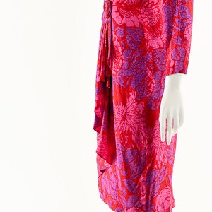 May include: A red and purple floral print dress with a ruffled skirt and long sleeves. The dress is on a white mannequin.