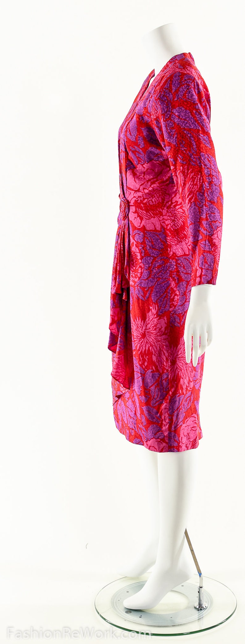 May include: A red and purple floral print dress with a ruffled skirt and long sleeves. The dress is on a white mannequin.