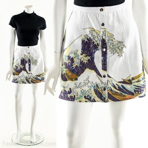 May include: A white mini skirt with a button-up front closure. The skirt features a colorful print of the Great Wave off Kanagawa, a famous Japanese woodblock print by Hokusai.