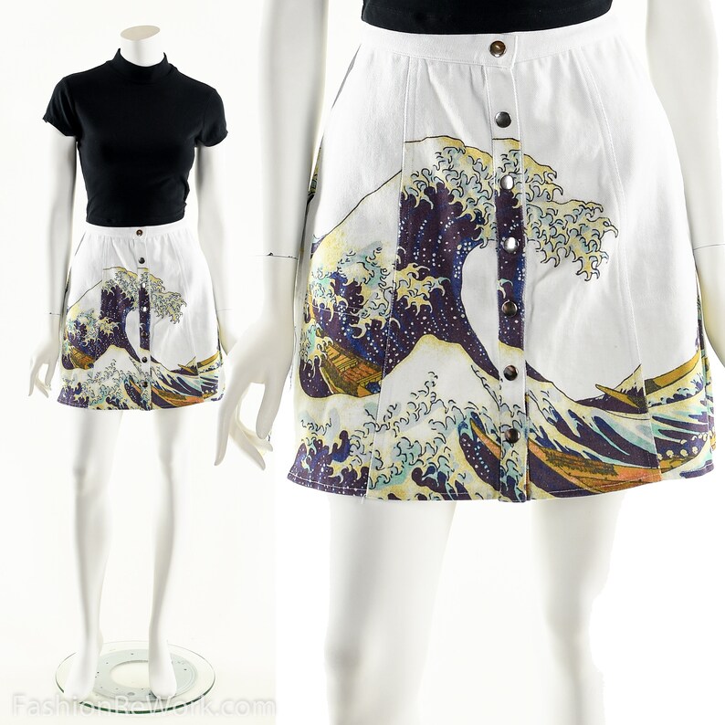 May include: A white mini skirt with a button-up front closure. The skirt features a colorful print of the Great Wave off Kanagawa, a famous Japanese woodblock print by Hokusai.