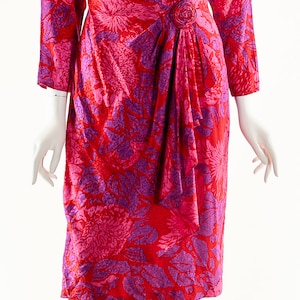 May include: A red and purple floral print wrap dress with a long sleeve and a button detail at the waist.