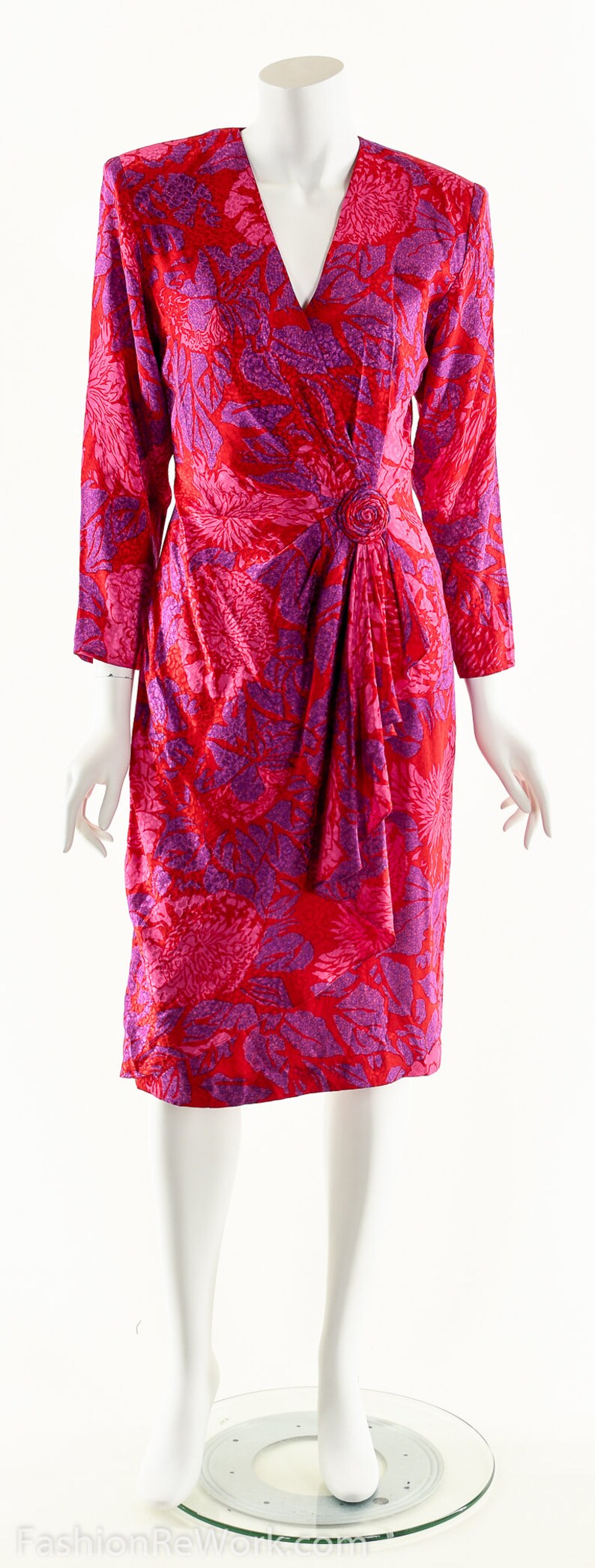 May include: A red and purple floral print wrap dress with a long sleeve and a button detail at the waist.