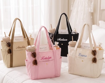 Könnte beinhalten: Vier Tragetaschen aus Segeltuch in Beige, Rosa, Schwarz und Cremeweiß, jeweils mit einer Vordertasche mit goldenem Druckknopf, zwei Henkeln und gestickten Namen: Amelia, Katelyn, Madison und Emma. Jede Tasche enthält einen Becher und eine Sonnenbrille.