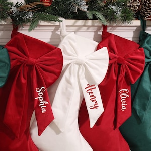 May include: Christmas stockings in red, white, and green velvet, each with a large bow and personalized name embroidery. Festive holiday decor with a star-shaped gingerbread cookie and pine boughs.