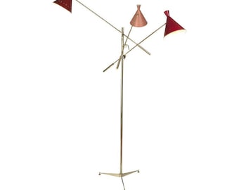 May include: A mid-century modern floor lamp with a brass finish and three adjustable lights. The conical shades are red, and the lamp has a tripod base. The lamp is designed for ambient lighting.
