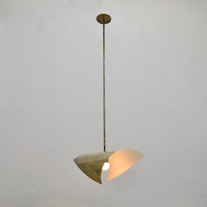 May include: A brass pendant light with a distinctive, curved shade. The shade features a warm, off-white interior and a metallic exterior. The light hangs from a slender rod and a circular ceiling mount.