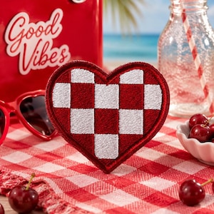 May include: A heart-shaped embroidered patch featuring a red and white checkered pattern. The patch has a thick red border and a textured surface created by the embroidery stitching, showcasing a classic woven-style grid design in vibrant colors.