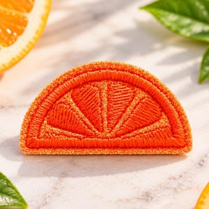 May include: A semi-circular orange slice patch featuring vibrant orange embroidery with detailed segment lines and a textured border, designed as a decorative applique with a bright citrus color palette and a clean, stitched finish.