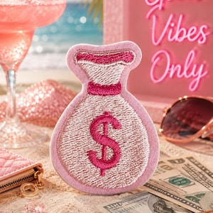 May include: A light pink embroidered patch shaped like a money bag with a dark pink dollar sign symbol in the center. The patch features a stitched border and a cinched top design, rendered in a soft fabric texture with detailed thread work.