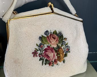May include: A white beaded evening bag with a gold clasp and a floral design. The bag has a long strap.
