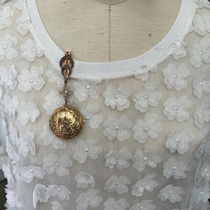 May include: A set of three ceramic mugs with a speckled, cream-colored glaze. Each mug features a different hand-painted floral design in shades of blue, green, and yellow. The mugs have a simple, rounded shape.