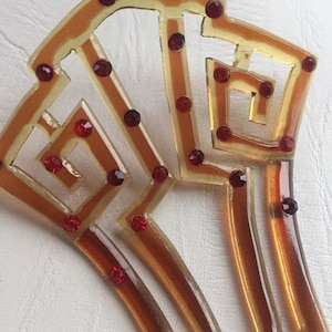 May include: A vintage amber plastic hair comb with a geometric design and red rhinestones.