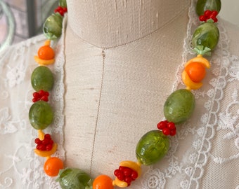 May include: A green, orange, and red fruit-shaped beaded necklace. The necklace is made of plastic and has a retro look.