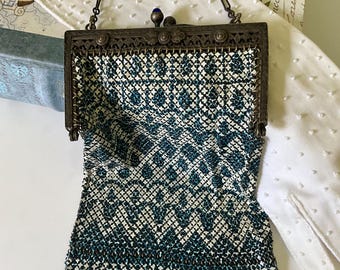 May include: An antique beaded handbag with a dark metal frame and chain handle. The bag features a geometric pattern in teal and white, with a scalloped edge. A small blue gem adorns the clasp.