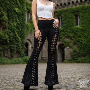 May include: Black flared pants with lace-up detailing along the sides. The pants have a high waist and a wide leg opening. The image shows the pants in an outdoor setting. The pants are part of a gothic fashion collection.