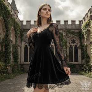 May include: A black velvet dress with long, sheer lace sleeves and a lace trim hem. The dress has a V-neckline and a fitted bodice that flares into a skirt. The dress is worn in front of a stone building.
